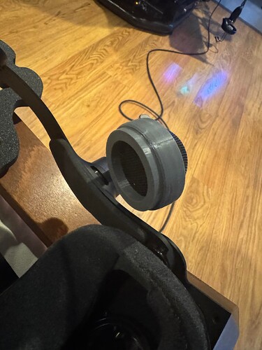 A close-up view of a 3D-printed attachment on a virtual reality headset, resting on a wooden floor with a VR setup visible in the background. (Captioned by AI)