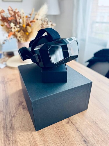 A black VR headset sits atop a dark gray box on a wooden table. (Captioned by AI)
